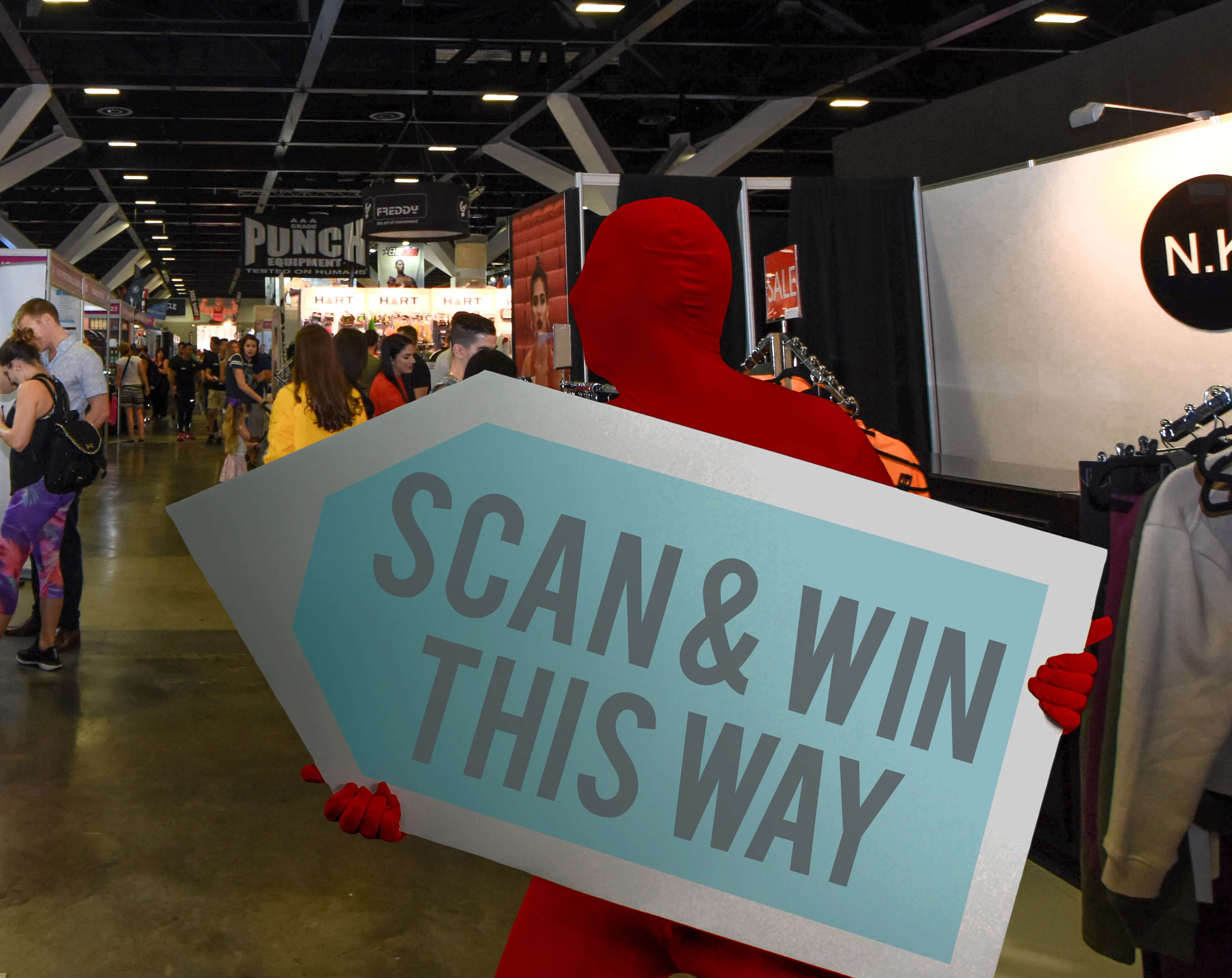 A sign waver holding a large arrow sign while wearing a bright red morph suit during an event