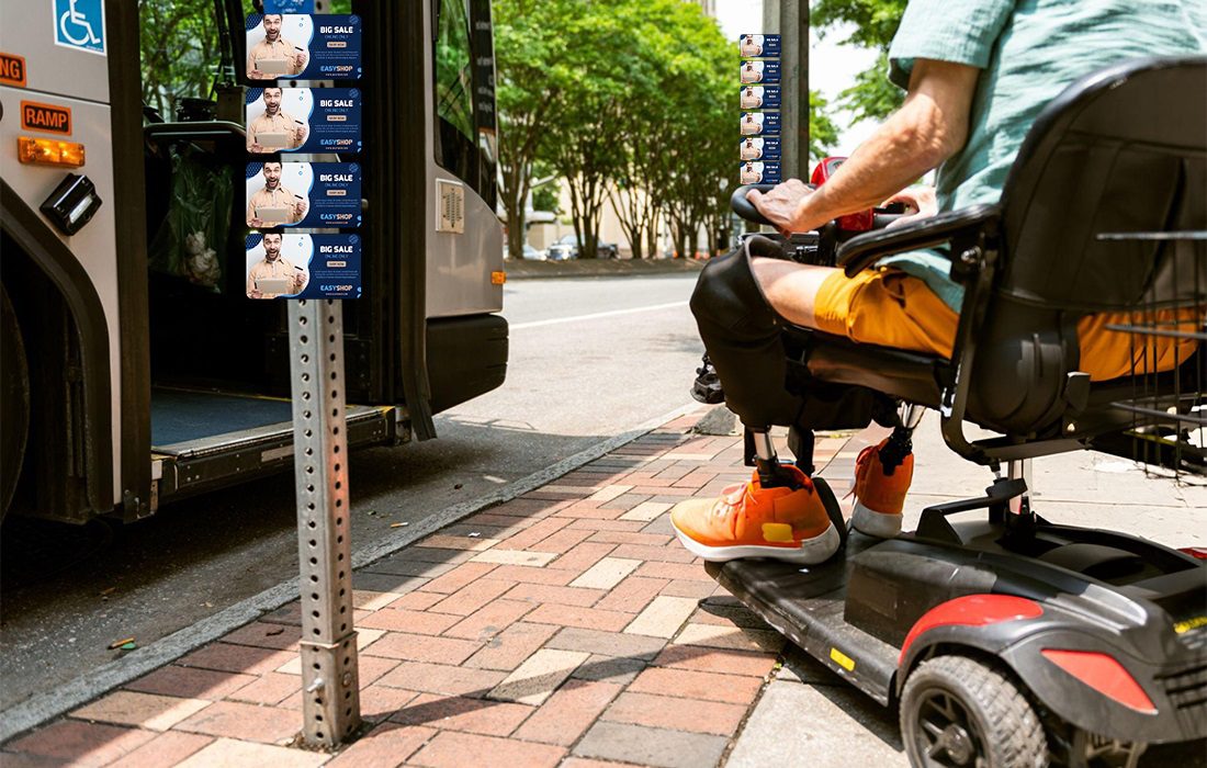 A men in a wheelchair boarding a bus next to a street sign covered in magnet bombing