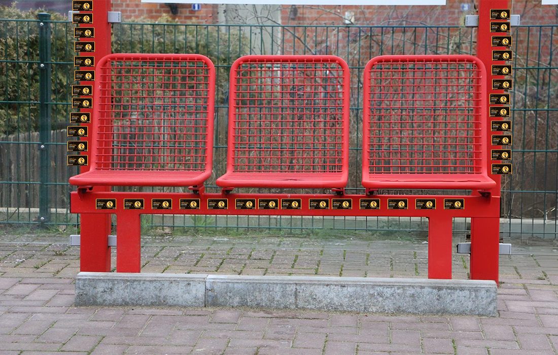 A red bus stop seat that has magnet bombing surrounding the metal frame